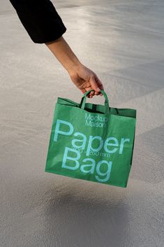 a person holding a green paper bag in their hand on top of the sand at the beach