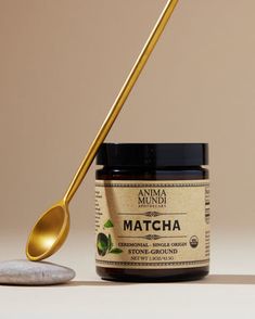 a jar of matcha next to a gold spoon on a white surface with a brown background