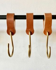 three hooks are hanging on the wall with brown leather straps attached to them and one hook is holding an umbrella