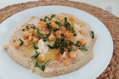 a white plate topped with hummus and garnish on top of a woven place mat