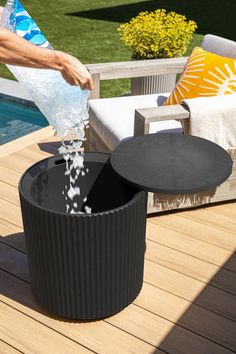 a person is pouring water into a black trash can on a wooden deck next to a swimming pool