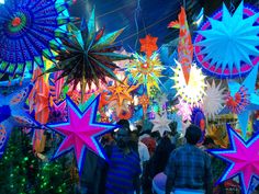 people are walking through an outdoor market with brightly colored paper stars hanging from the ceiling