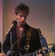 a man with a guitar in front of a microphone and another person standing behind him