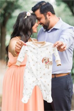 a man and woman holding up a baby's pajamas