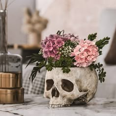 a skull vase with flowers in it sitting on a marble counter top next to a candle holder