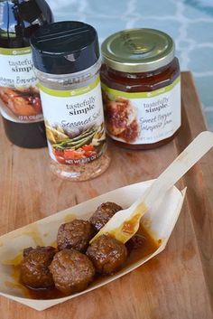 some food is sitting on a wooden tray next to two jars of jam and a spoon