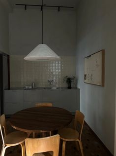 a dining room table and chairs in front of a kitchen with an overhead light hanging over it