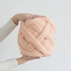 a ball of pink yarn being held by two hands with white walls in the background