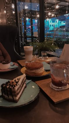 desserts and drinks are sitting on the table in front of a window at night