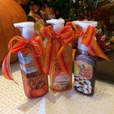 three bottles with orange ribbons tied around them sitting on a table next to pumpkins