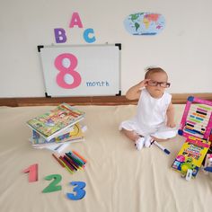 a baby sitting on a bed surrounded by toys and books with the number eight behind it