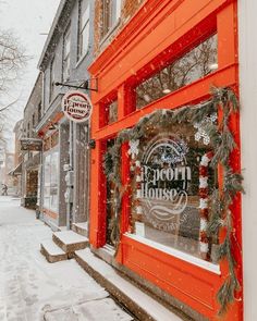 an orange store front with christmas decorations on the windows and snow covered sidewalk in front