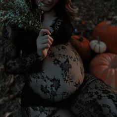 a pregnant woman is sitting on the ground with flowers in her hand and pumpkins behind her