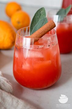 two glasses filled with drinks and garnished with cinnamon on the rim, sitting next to oranges