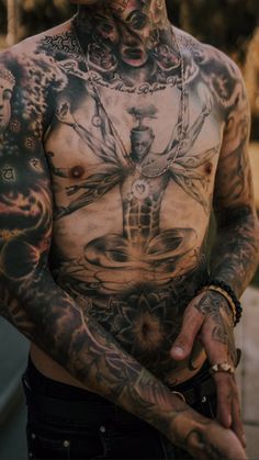 a man with many tattoos on his body and chest standing in front of a tree