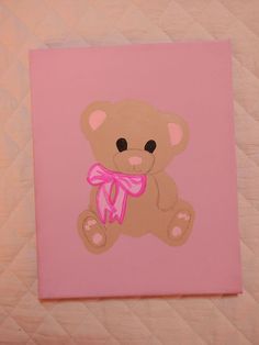 a brown teddy bear with a pink bow sitting on top of a quilted bed