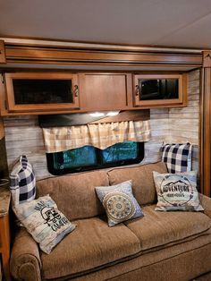 a couch with pillows on it in front of a kitchen and living room inside an rv