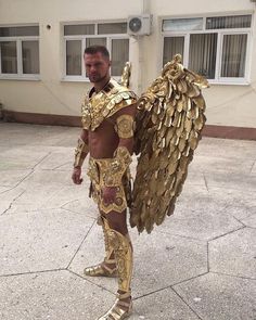 a man dressed in gold with wings on his chest and arms, standing outside wearing an elaborate golden costume