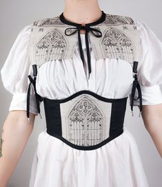 A corset-belt of midnight black linen featuring a single front panel of a Gothic cathedral window against an oatmeal background.Inspired by the ethereal elegance of medieval architecture & Victorian gothic aesthetics. This piece laces up at the center back through black steel eyelets. The exterior is made from new linen (a sustainable textile) while the lining is made from upcycled fabric. Pictured with the Silk Chemise and the Cathedral PartletAvailable in Small, Medium, Large and Extra Lar Cathedral Fashion, Architecture Victorian, Dramatic Dress, Wearable Sculpture, Belt Corset, Dramatic Dresses, Wedding Corset, Ethereal Elegance, Costume Sewing