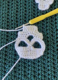 two crocheted masks are sitting next to a knitting needle on a green blanket