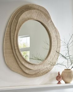 a round mirror sitting on top of a white mantle next to a vase and potted plant