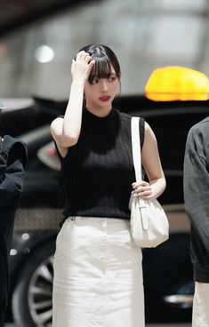 a woman in white skirt and black top walking down the street with her hand on her head