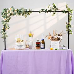 a table topped with bottles and flowers next to a purple table cloth covered tablecloth