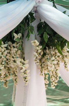 white flowers and greenery are hanging from the back of a wedding arch with draping