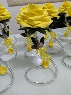 yellow flowers are in clear vases on a table with silver rings and beads around them