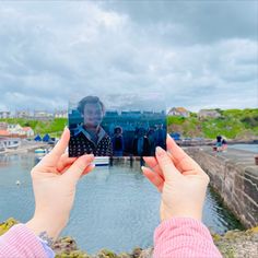 two hands holding up a polaroid with people in the background and water behind them