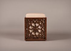 an intricately carved wooden box with a cushion on it's side, against a gray background