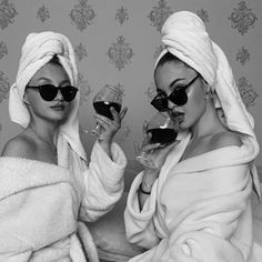 two women in bathrobes drinking wine and holding glasses with their faces covered by towels