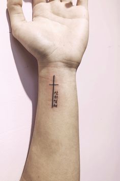 a person's arm with a cross tattoo on the left side of their wrist