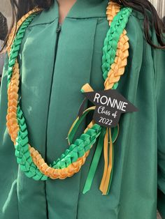 a woman wearing a green graduation gown with a name tag attached to her neck and braids around the neck