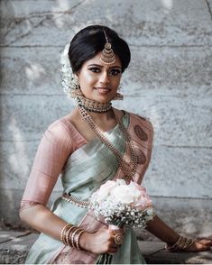 a woman in a green and pink sari holding a bouquet of flowers on her left hand