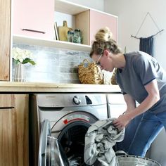 a woman is doing laundry in the kitchen with her washing machine and basket next to it