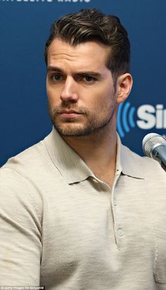 a man sitting in front of a microphone with his hand on his hip and looking at the camera