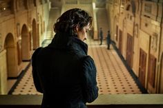 a woman standing in an old building looking out at the floor and stairs, with her back turned to the camera