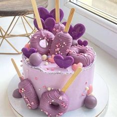 a pink cake with purple frosting and hearts on top is sitting in front of a window