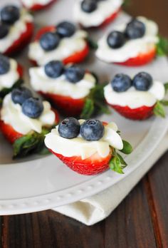 some strawberries and blueberries are on a white plate with cream cheese frosting