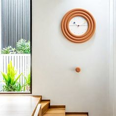 a clock mounted to the side of a wall next to some steps and plants in a room