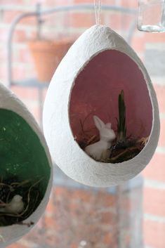 two hanging bird feeders filled with plants and birds in the nest, one has a white rabbit inside