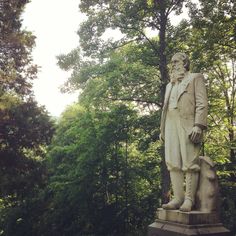 a statue of a man with a dog in his hand and trees behind him on a sunny day