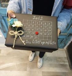 a person holding a box with a calendar on it and a flower in the middle