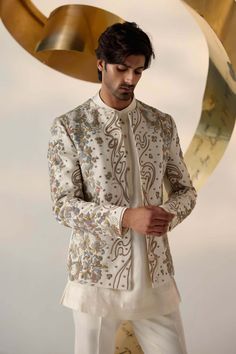 Editor's Note Featuring our infamous short jacket silhouette in dirty ivory color. Hand-embroidered with colorful reshams, gold zari, dabka, and twisted lines. Paired with a short-length potli button kurta and tapered trousers. Fabric: Linen silk Color: Ivory Components: Short jacket, kurta and trousers Occasion: Groom Fit: Regular Note: Product colour may slightly vary due to photographic lighting sources Care: Dry clean only About the Designer After establishing himself as the leading couturie Indian Men Wedding Outfit Groom Attire, Nawabi Style Men, Traditional For Men, Men In Traditional, Jatin Malik, Indian Wedding Suits Men, Potli Button, Jacket Silhouette, Indian Wedding Clothes For Men