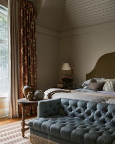 a large bed sitting next to a window in a room with curtains on the windowsill