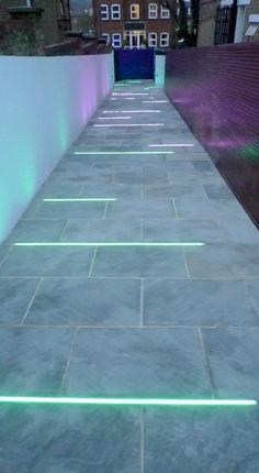 a long walkway with green lights on the side and buildings in the backround