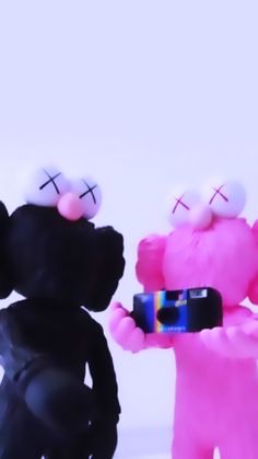 two black and pink teddy bears with cell phones in their hands, one holding a camera