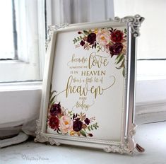 a framed sign with flowers on it sitting next to a white window sill in front of a window