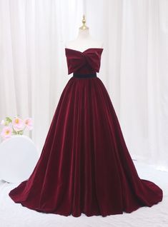 Accentuate your elegance in this stunning burgundy prom dress! Crafted from luxurious velvet, this gown exudes sophistication with its deep red hue and sumptuous texture. The bodice features a unique bow-like detail at the neckline, creating a striking focal point that is both modern and chic. The waist is cinched with a sleek black band, enhancing the natural silhouette and leading to a full, flowing skirt that gracefully sweeps the floor as you move. Perfect for a prom or a formal evening event, this dress is designed to make a bold statement. Its timeless color and refined design ensure you will turn heads, while its classic cut provides comfort and style in equal measure. Red Dress With Bow, Bow Prom Dress, Prom Dress Burgundy, Burgundy Prom, Unique Bows, Velvet Prom Dress, Princess Prom Dresses, Strapless Prom Dress, Velvet Gown